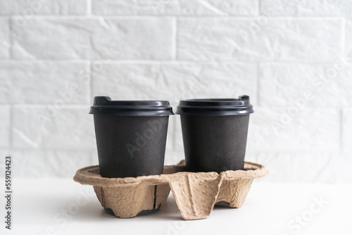 Takeaway paper coffee cups in cardboard holder on wooden table against black background, space for text.