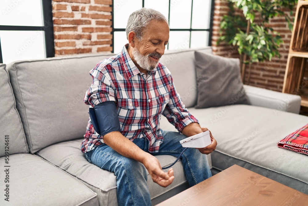 Fototapeta premium Senior grey-haired man measuring pulse using tensiometer at home