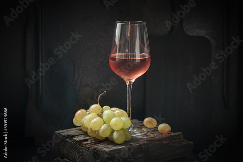 Glass of rose wine with ripe white grapes on dark background still life with copy space. Drinking wine concept photo