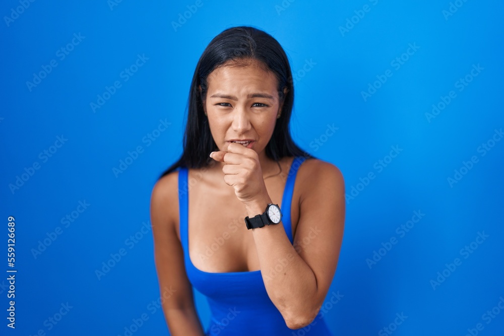 Hispanic woman standing over blue background feeling unwell and coughing as symptom for cold or bronchitis. health care concept. Hispanic woman standing over blue background feeling unwell and coughing as symptom for cold or bronchitis. health care concept.