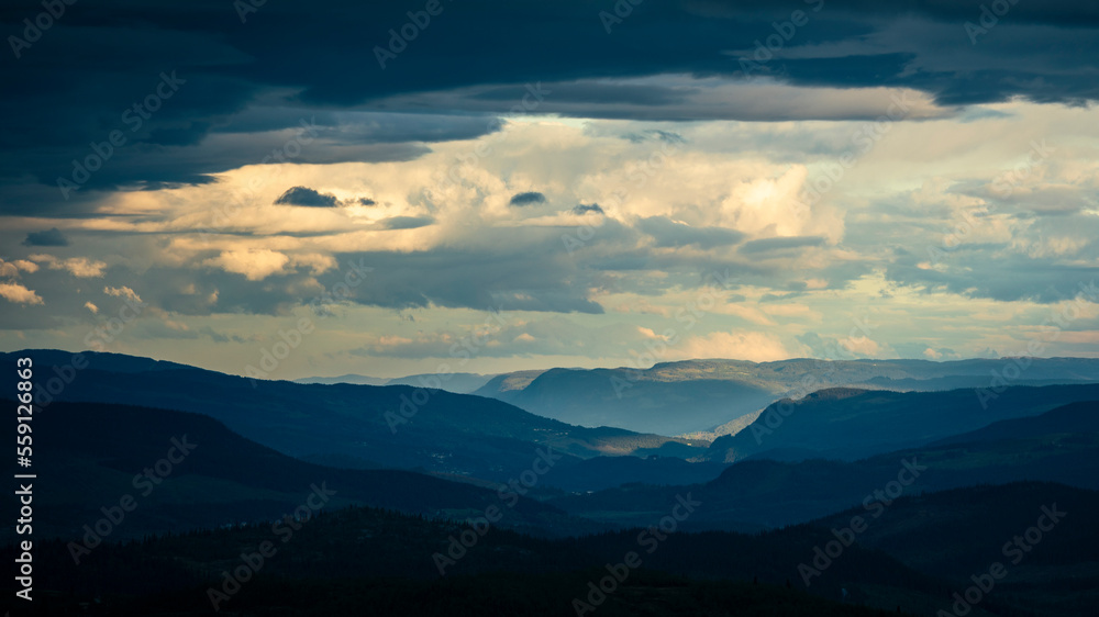 Mountain silhouette layers in the landscape of Jotunheimen National Park in Norway, dark and colorful clouds in the sky