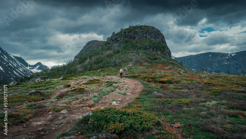 Woman hiking in mountain landscape to Knutshoe summit in Jotunheimen National Park in Norway, colorful moss and vegetation in foreground, mountains of Besseggen in the background photo