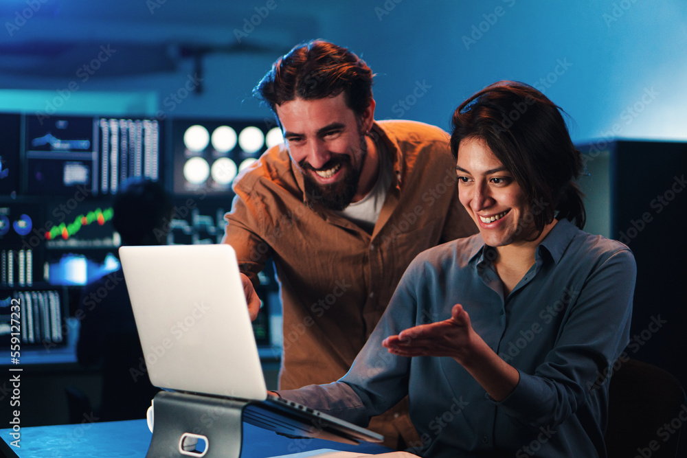 Happy business couple working on a laptop computer in the office. Young trading team people smiling watching data on pc screen. Two partners coworking on finance. High quality photo Happy business couple working on a laptop computer in the office. Young trading team people smiling watching data on pc screen. Two partners coworking on finance. High quality photo