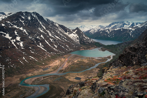 Turquoise lakes and river in mountain landscape from above the hike to Knutshoe summit in Jotunheimen National Park in Norway, snow-covered mountains of Besseggen in background