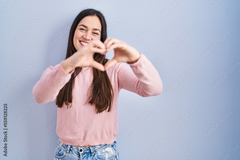 Young brunette woman standing over blue background smiling in love doing heart symbol shape with hands. romantic concept. Young brunette woman standing over blue background smiling in love doing heart symbol shape with hands. romantic concept.