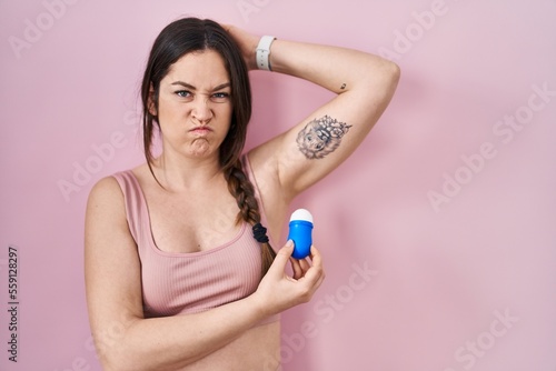 Young brunette woman using roll on deodorant skeptic and nervous  frowning upset because of problem. negative person.