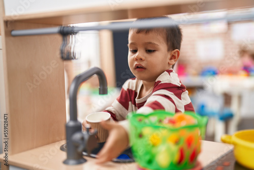 Adorable toddler playing with play kitchen standing at kindergarten photo