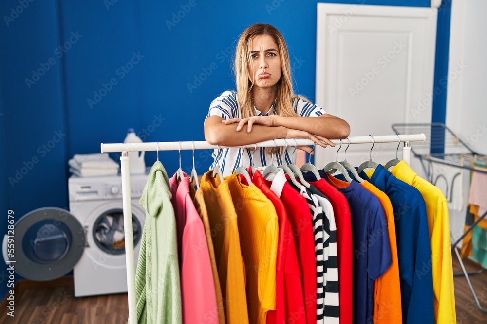Young blonde woman at laundry room with clean clothes depressed and worry for distress, crying angry and afraid. sad expression. Young blonde woman at laundry room with clean clothes depressed and worry for distress, crying angry and afraid. sad expression.