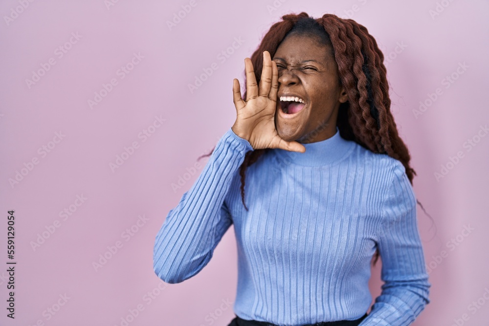 African woman standing over pink background shouting and screaming loud to side with hand on mouth. communication concept. African woman standing over pink background shouting and screaming loud to side with hand on mouth. communication concept.