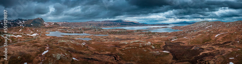 Panorama landscape with blue lakes, mountains and road of Jotunheimen National Park in Norway from above, dramatic dark cloudy sky