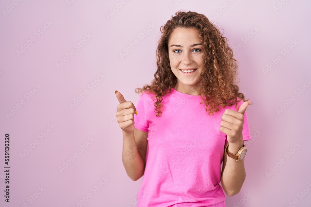 Young caucasian woman standing over pink background success sign doing positive gesture with hand, thumbs up smiling and happy. cheerful expression and winner gesture. Young caucasian woman standing over pink background success sign doing positive gesture with hand, thumbs up smiling and happy. cheerful expression and winner gesture.