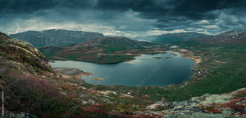 Mountain landscape with lake Nedre Leirungen from above the hike to Knutshoe summit in Jotunheimen National Park in Norway, mountains of Besseggen in background, dark cloudy sky