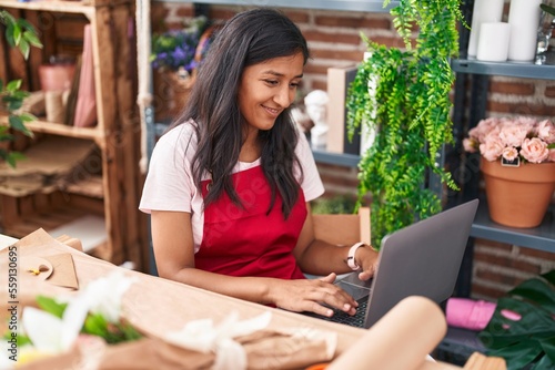 Young beautiful hispanic woman florist smiling confident using laptop at flower shop