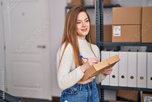 Young blonde woman ecommerce business worker writing on package at office