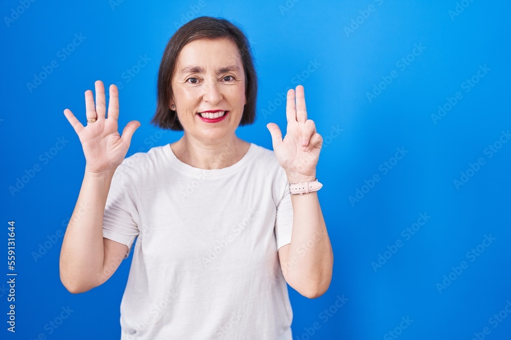 Middle age hispanic woman standing over blue background showing and pointing up with fingers number eight while smiling confident and happy. Middle age hispanic woman standing over blue background showing and pointing up with fingers number eight while smiling confident and happy.
