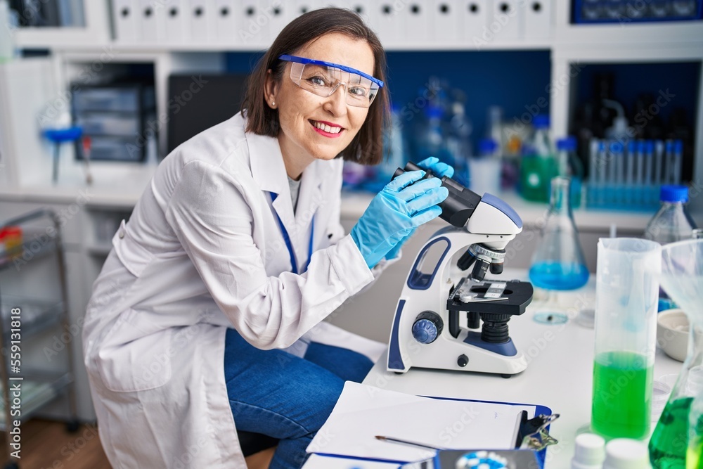 Middle age woman scientist smiling confident using microscope at laboratory Middle age woman scientist smiling confident using microscope at laboratory