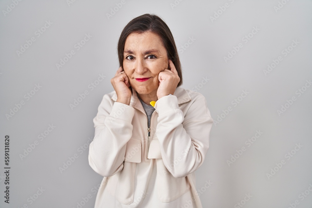 Middle age hispanic woman standing over isolated background covering ears with fingers with annoyed expression for the noise of loud music. deaf concept. Middle age hispanic woman standing over isolated background covering ears with fingers with annoyed expression for the noise of loud music. deaf concept.