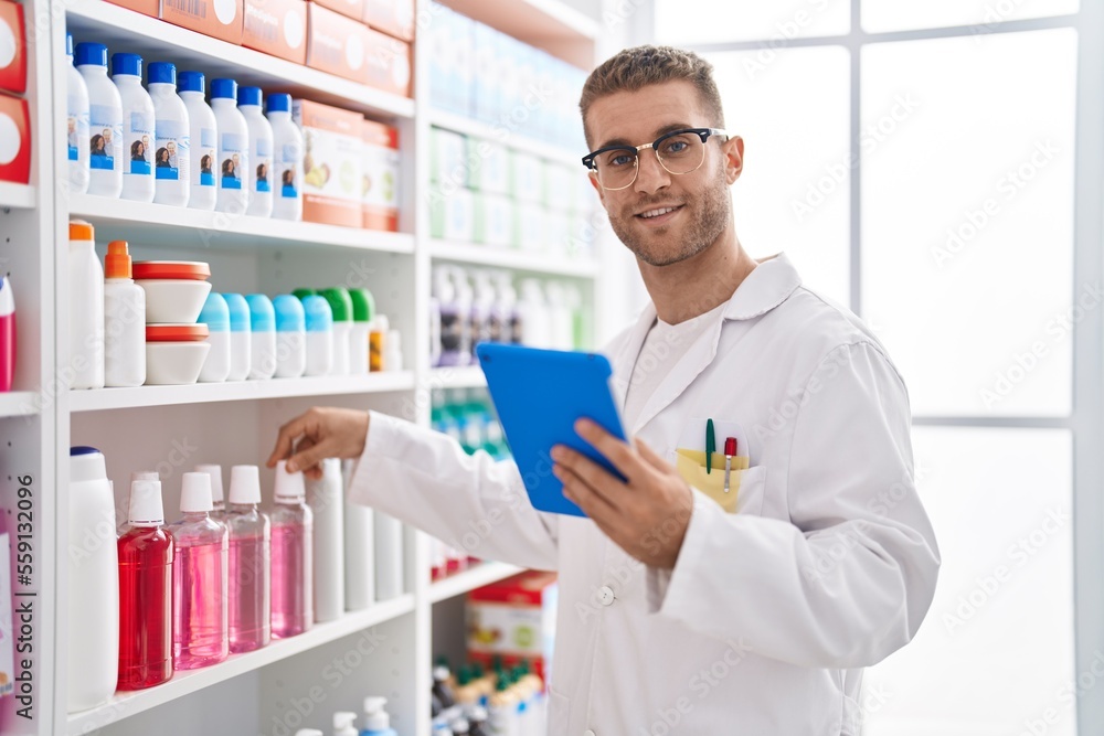 Young caucasian man pharmacist using touchpad working at pharmacy