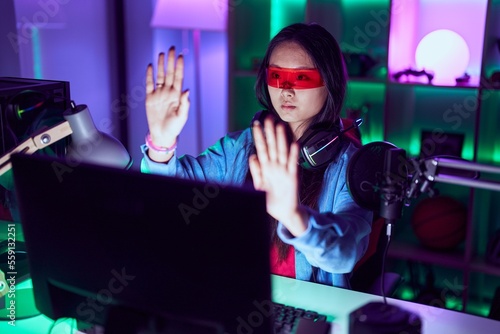 Young chinese woman streamer playing video game using virtual reality glasses at gaming room