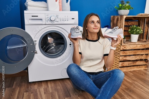 Young woman putting sneakers in washing machine smiling looking to the side and staring away thinking.