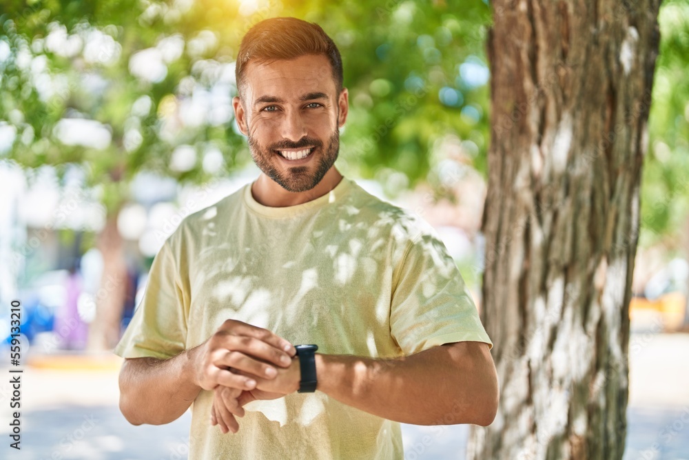 Obraz premium Young hispanic man smiling confident looking watch at park