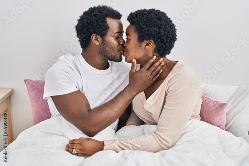 African american man and woman couple hugging each other and kissing sitting on bed at bedroom