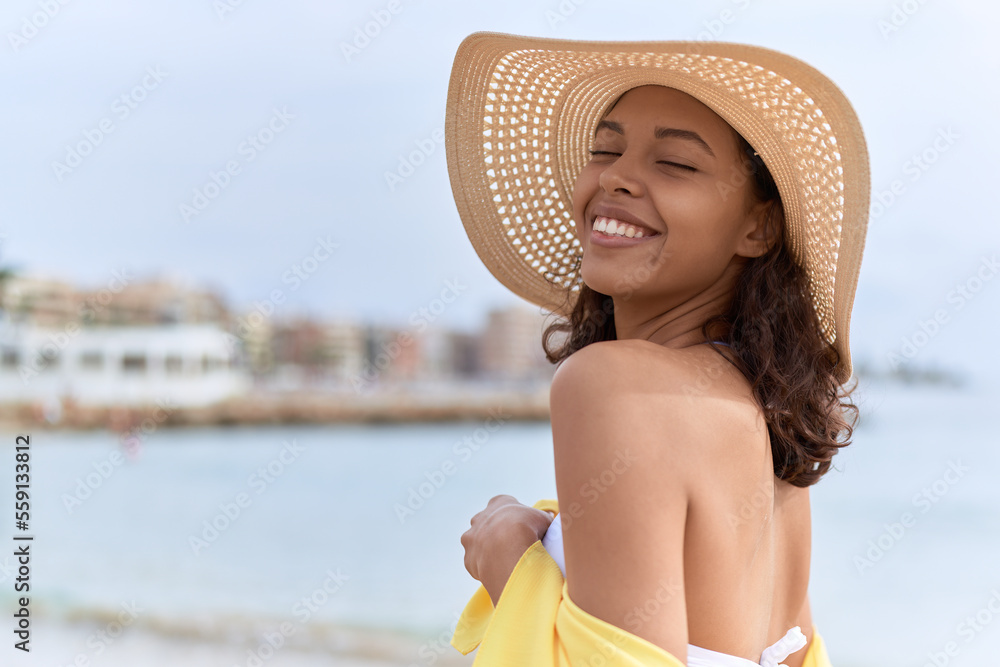 Young african american woman smiling confident wearing summer hat and bikini at beach