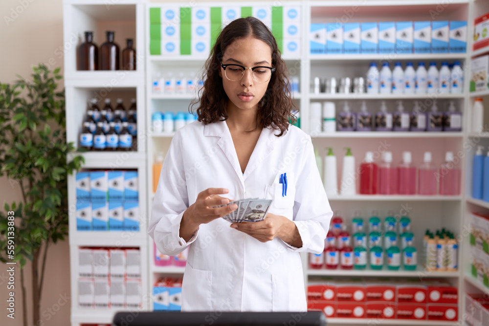 Young african american woman pharmacist counting dollars at pharmacy