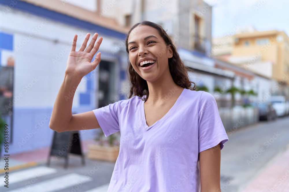 Young african american woman smiling confident saying hello with hand at coffee shop terrace