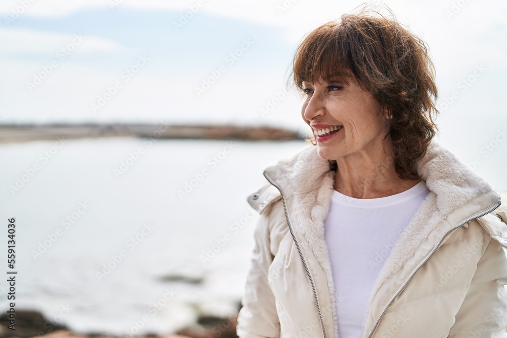Middle age woman smiling confident looking to the side at seaside Middle age woman smiling confident looking to the side at seaside