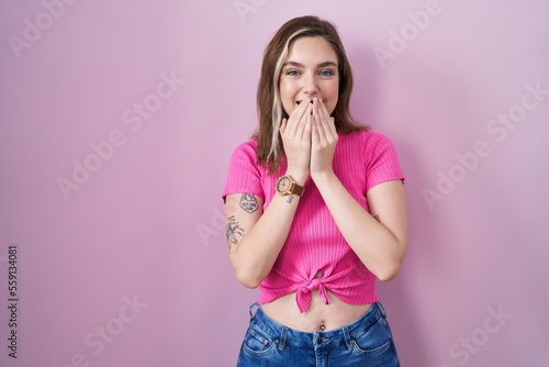 Foto Blonde caucasian woman standing over pink background laughing and embarrassed gi