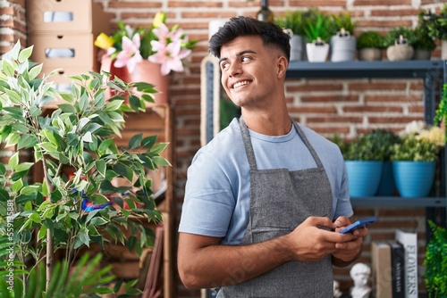 Young hispanic man florist smiling confident using smartphone at flower shop