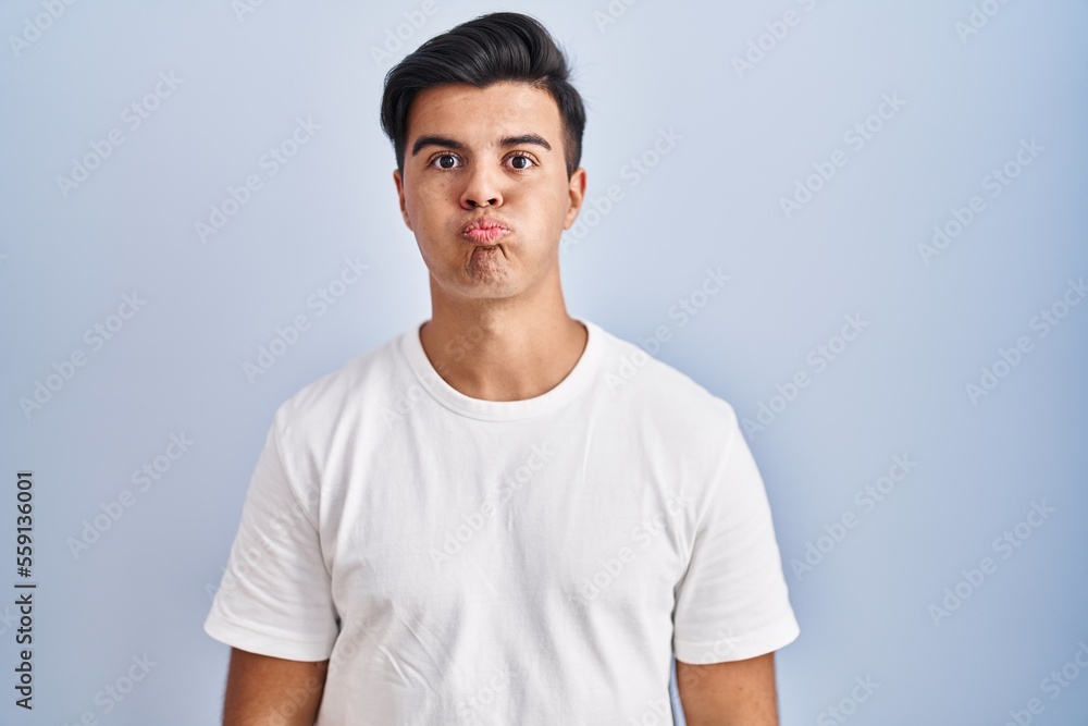 Hispanic man standing over blue background puffing cheeks with funny face. mouth inflated with air, crazy expression. Hispanic man standing over blue background puffing cheeks with funny face. mouth inflated with air, crazy expression.
