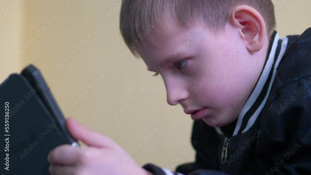 portrait of an attractive caucasian boy 7-9 years old uses a tablet while inside. the child uses the Internet on a tablet device. the student has fun on the tablet portrait of an attractive caucasian boy 7-9 years old uses a tablet while inside. the child uses the Internet on a tablet device. the student has fun on the tablet
