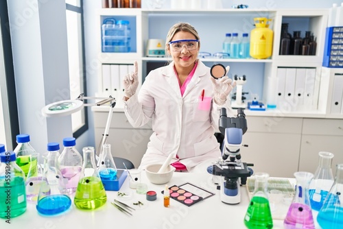 Young hispanic woman working at scientist laboratory doing make up surprised with an idea or question pointing finger with happy face  number one
