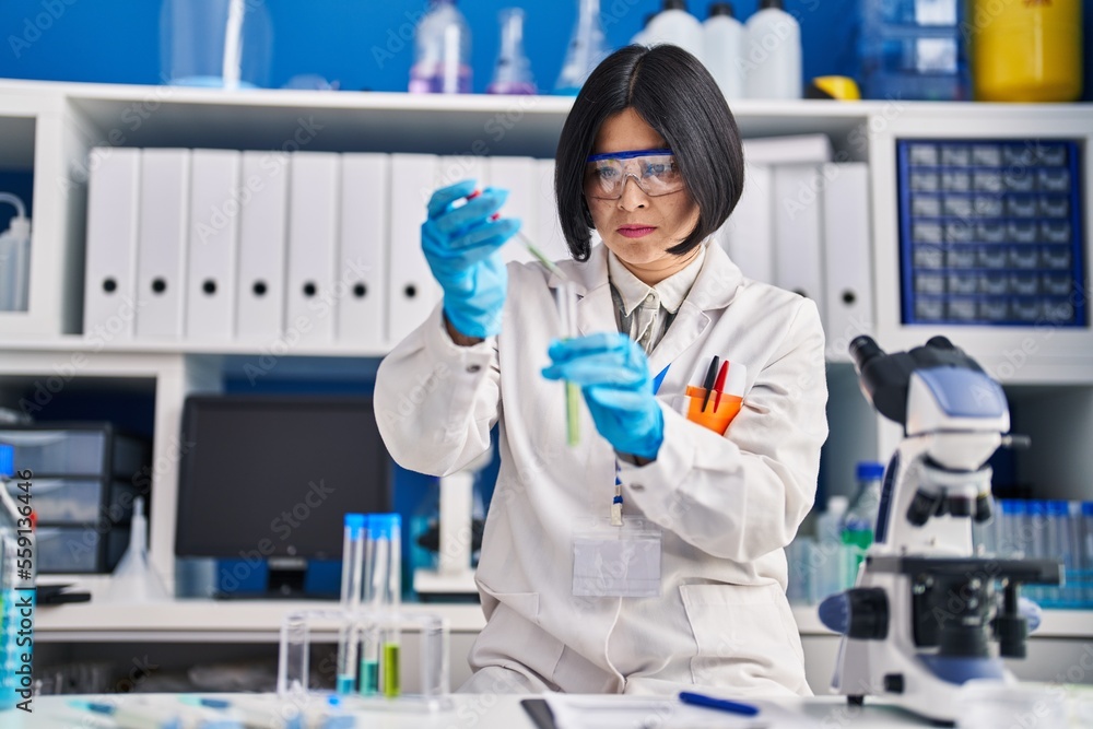 Young chinese woman scientist pouring liquid on test tube at laboratory