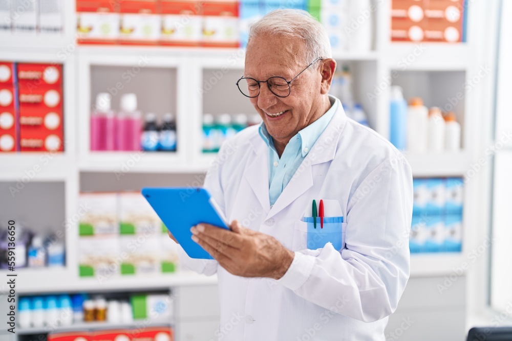 Senior grey-haired man pharmacist using touchpad at pharmacy Senior grey-haired man pharmacist using touchpad at pharmacy