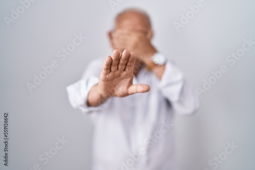 Senior man with grey hair standing over isolated background covering eyes with hands and doing stop gesture with sad and fear expression. embarrassed and negative concept.