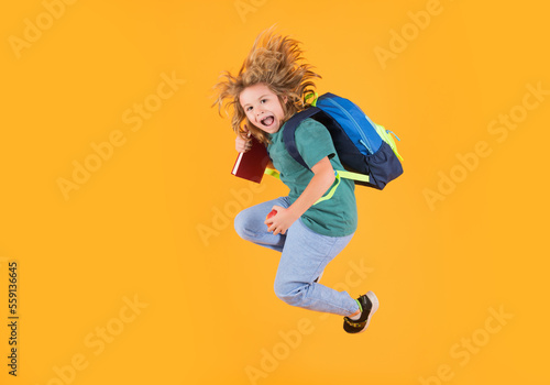 Full length of excited kid jumping. Back to school. Full length body of little school kid jumping having fun isolated yellow color background. Crazy school boy jump.
