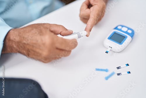 Senior grey-haired man measuring glucose sitting on table at home