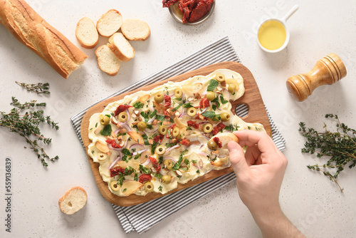 Trendy Butter Board with olives, sun-dried tomatoes, nuts, thyme, red onion and herbs with crispy baguette on white background, View from above. Man testing and eating butterboard. photo