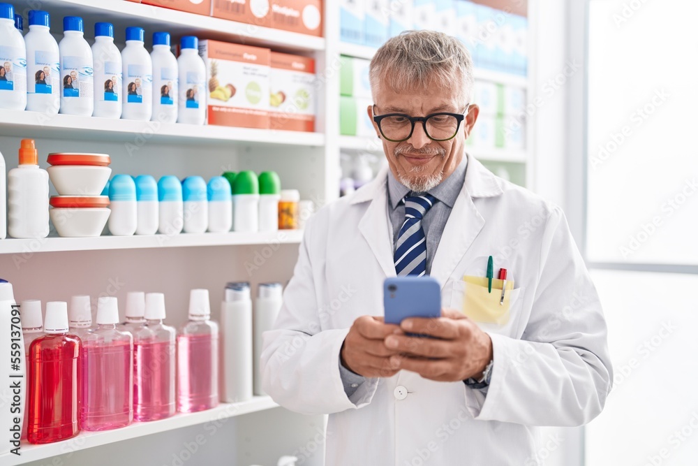 Middle age grey-haired man pharmacist using smartphone working at laboratory