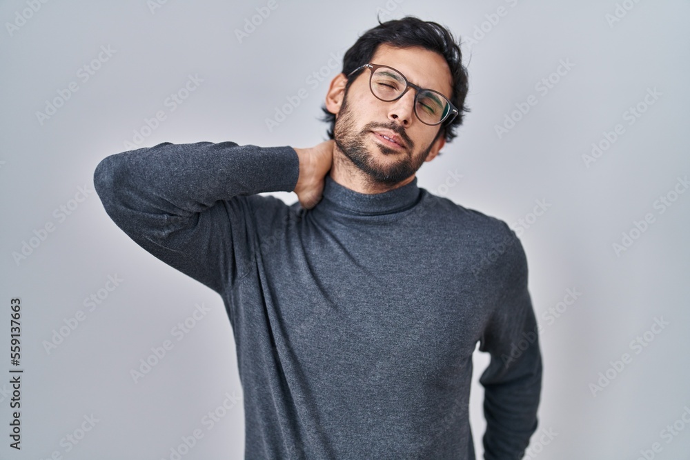 Handsome latin man standing over isolated background suffering of neck ache injury, touching neck with hand, muscular pain Handsome latin man standing over isolated background suffering of neck ache injury, touching neck with hand, muscular pain
