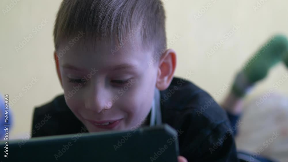 attractive caucasian boy 8 years old uses a tablet lying at home looking at the screen in surprise. emotions of children concept, children's content, entertainment on the tablet attractive caucasian boy 8 years old uses a tablet lying at home looking at the screen in surprise. emotions of children concept, children's content, entertainment on the tablet