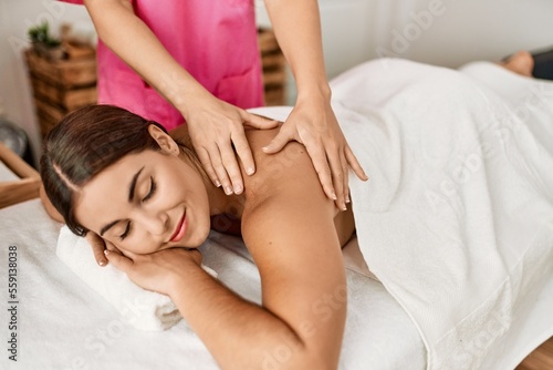 Young beautiful hispanic woman lying on table having back massage at beauty salon