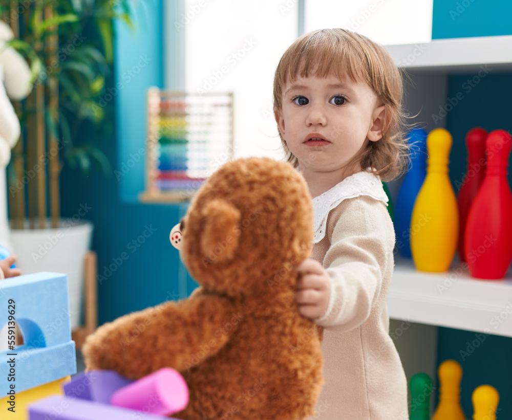 Adorable hispanic girl holding doll standing at kindergarten Adorable hispanic girl holding doll standing at kindergarten