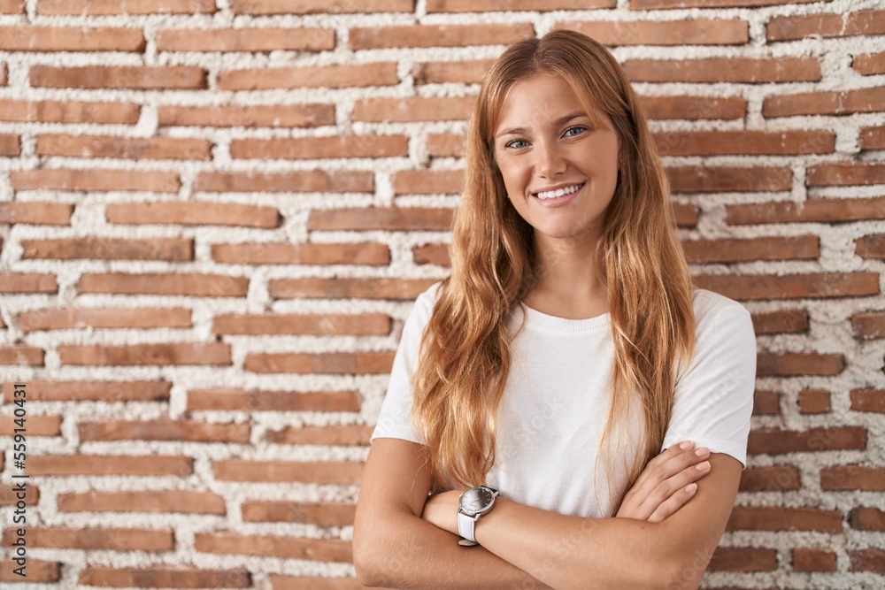 Young caucasian woman standing over bricks wall happy face smiling with crossed arms looking at the camera. positive person. Young caucasian woman standing over bricks wall happy face smiling with crossed arms looking at the camera. positive person.