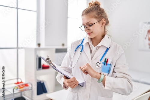 Young blonde woman doctor reading medical report at clinic