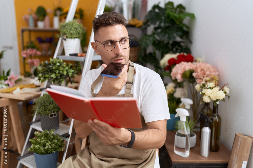 Young hispanic man florist talking on smartphone reading book at flower shop Young hispanic man florist talking on smartphone reading book at flower shop