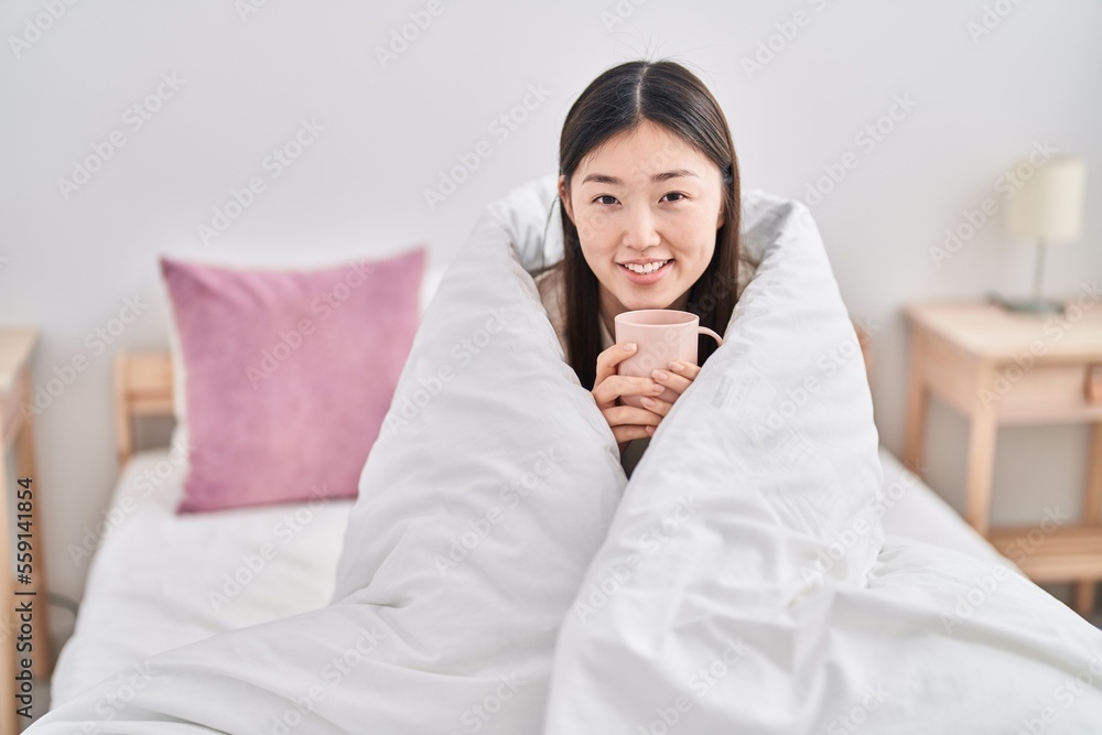 Chinese woman drinking cup of coffee covering with bedsheet at bedroom Chinese woman drinking cup of coffee covering with bedsheet at bedroom